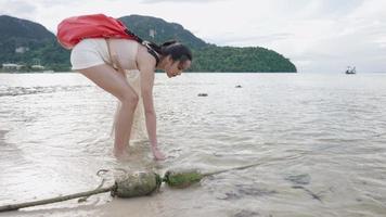 aziatische jonge vrouw die het vuile strand opruimt door zelf een plastic zak met alcoholfles te verzamelen, vuilnis op te halen als vrijwilliger voor afvalrecycling. ecologie milieubewustzijn, veilige planeet video