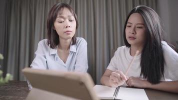 nachdenkliche junge asiatische Studentin, die ernsthaft versucht, eine Online-Lektion zu verstehen, glückliche Cousine, die ihrer kleinen Schwester hilft, sich auf die Universitätsprüfung vorzubereiten, gute Teamarbeit, Zugang zu digitalen Kenntnissen video