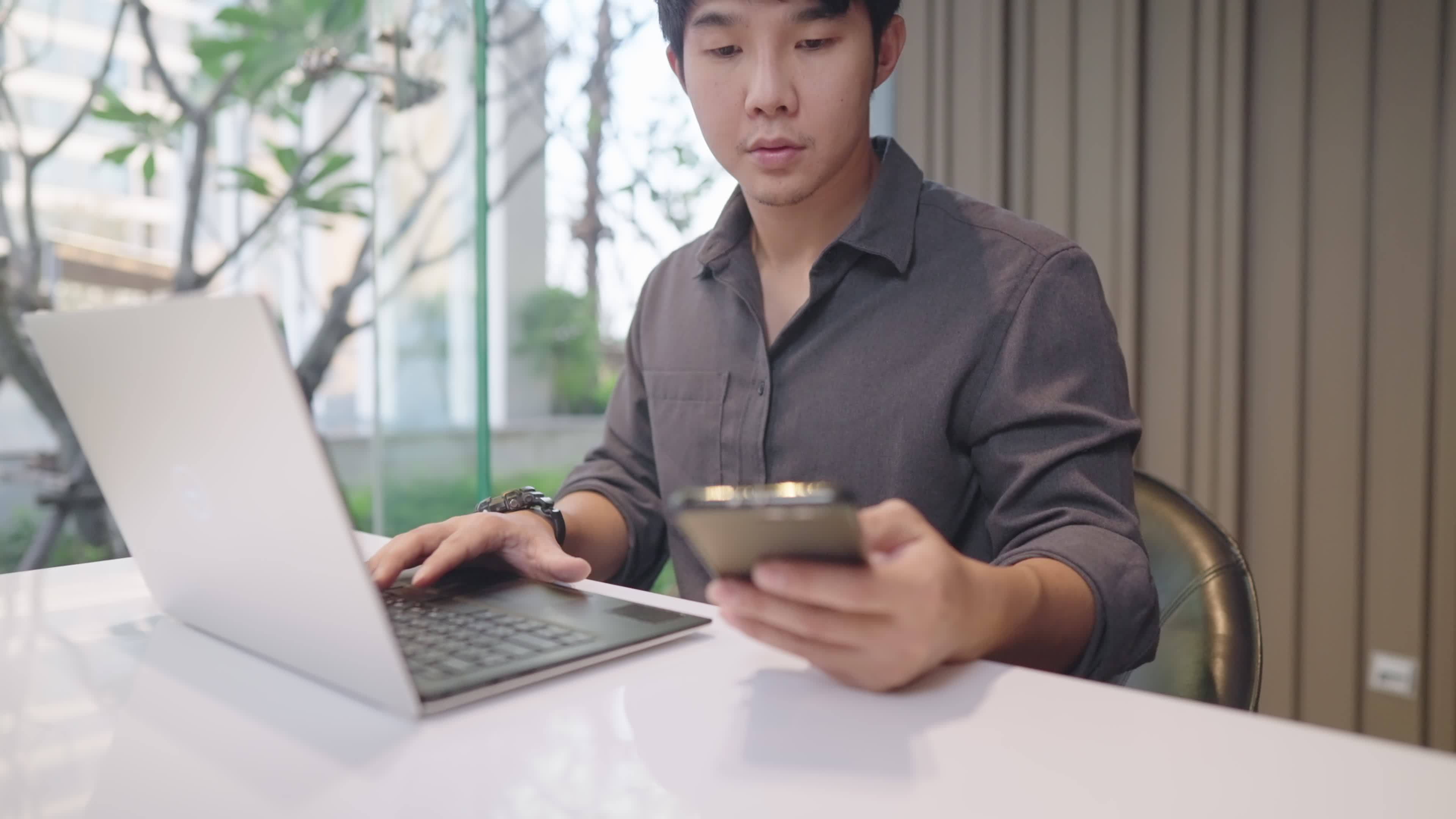 Asian freelancer talking to clients and working with the laptop computer at  the same time, young adult male using wireless technology for his  multitasking works, calling assistant for more information 7582809 Stock