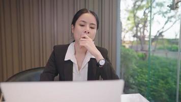 Thoughtful Asian business woman try to think of new idea to solve problem, concentrate focused thinking in front of laptop, young entrepreneur in formal suit attire sitting at remote working desk video