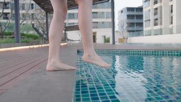 jovem linda pele clara pernas femininas entrando na piscina, viagem relaxante, férias no hotel, pele fina e macia, férias no resort de verão, descalço mergulhe na água clara da piscina, atividade ao ar livre, tiro de vista lateral video