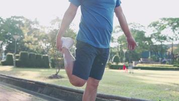 hombre asiático haciendo estiramiento de piernas de pie en el parque público antes del ejercicio, problema óseo del ligamento articular, levantando la pierna, prevención de lesiones, estilo de vida activo, calentamiento antes de correr, quema de calorías video