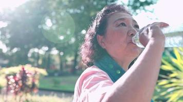 une femme asiatique d'âge moyen boit de l'eau fraîche à partir d'une bouteille en plastique après avoir fait de l'exercice dans le jardin du parc naturel, boisson rafraîchissante, réhydratation à la retraite, eau minérale h2o, rester hydraté vieillesse