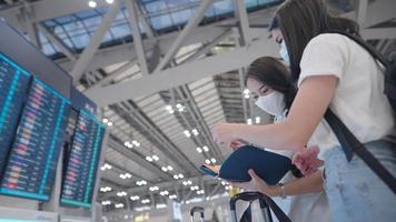 Two young asian women passengers standing in front of airport time schedule board and checking on travel itinerary  documents looking airline ticket check-in counter, international travel insurance video