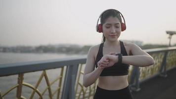 Slo-motion, an Asian sports woman wearing black sportswear, is running practicing, checking the watch every day in the morning in the river town before the marathon. video