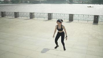 desportista asiática de câmera lenta vestindo roupas esportivas pretas pulando em uma escada de estiramento aquecer antes de correr uma maratona prática todos os dias de manhã na cidade com o rio antes da maratona. video