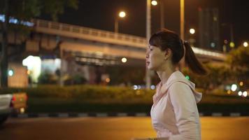 Slow-motion,Side Follow Camera View.Female athlete wearing a pink hoodie. Practice jogging at night every day. City streets with lots of lights in the background. Urban night jogging concept. video