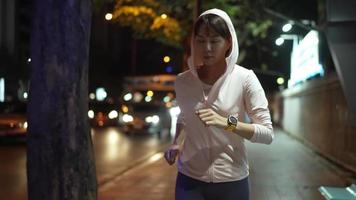 câmera lenta, fonte siga a câmera view.female atleta vestindo um capuz rosa. pratique jogging percorrendo o ponto de ônibus à noite todos os dias, as ruas da cidade com muitas luzes ao fundo. video