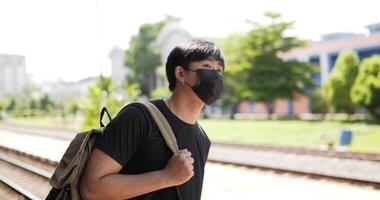 portret van de jonge aziatische reiziger die op de trein wacht op het treinstation. man met beschermende maskers, tijdens covid-19-noodsituatie. transport, reizen en social distancing concept. video