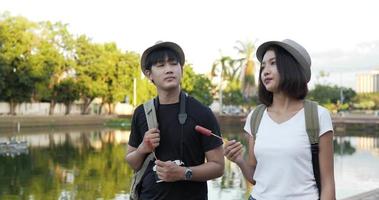 Side view of Happy Couple Asian with hat eating sausages while walking at the park. Cheerful Young man and woman eating an appetizing. Vacation and lifestyle concept. video