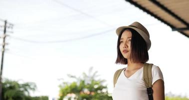 vue latérale d'une voyageuse asiatique fatiguée avec chapeau marchant et se reposant à la gare. femme utilisant un smartphone. concept de transport, de voyage et de technologie.
