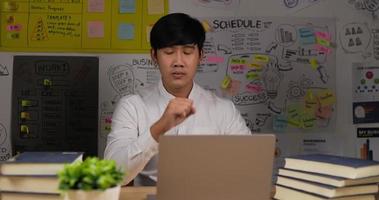 Das Porträt eines verschlafenen asiatischen Geschäftsmannes sitzt am Schreibtisch mit einem Laptop, der im Heimbüro arbeitet. müder mitarbeiter, der am arbeitsplatz in der nähe des laptops schläft, fühlt sich überarbeitet an. video