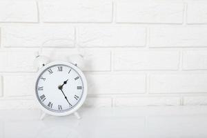 Retro alarm clock with twenty five minutes past one o'clock near brick wall on white workplace. Selective focus photo