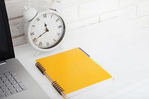 Retro alarm clock with notebook near brick wall on white workplace. Selective focus. Business concept. Copy space photo