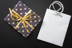 caja de regalo en lunares y bolsa de papel sobre fondo negro. vista superior y espacio de copia