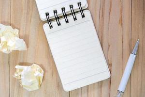 Small note book paper or notepad for writing information with color pen and crumpled paper balls on wooden table. view from above photo