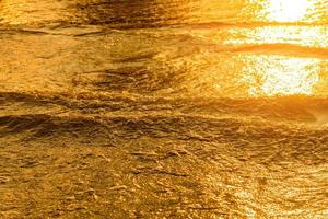 luz dorada que se refleja en una ola de agua en el mar y arena al atardecer. tono oro puro foto