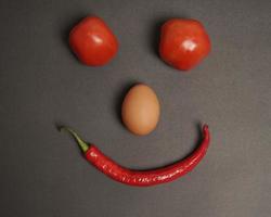 la combinación de tomates frescos, chiles rojos y huevos forma una cara sonriente. ingredientes de cocina listos para ser servidos. desenfoque de enfoque, inspiración de fondo. combinación de colores negro y rojo. foto