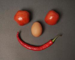 la combinación de tomates frescos, chiles rojos y huevos forma una cara sonriente. ingredientes de cocina listos para ser servidos. desenfoque de enfoque, inspiración de fondo. combinación de colores negro y rojo. foto