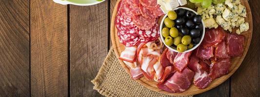 Antipasto catering platter with bacon, jerky, salami, cheese and grapes on a wooden background photo