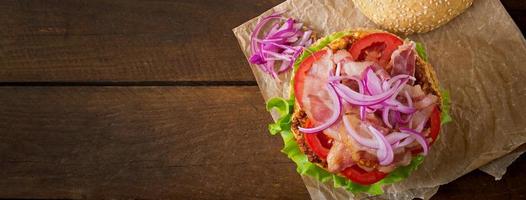 sándwich grande - hamburguesa con carne de res, cebolla roja, tomate y tocino frito. foto