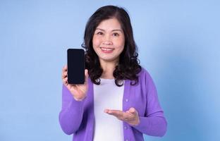 Portrait of middle aged Asian woman using smartphone on blue background photo