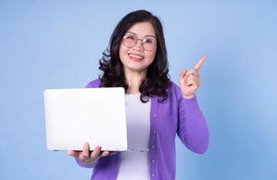 Portrait of middle aged Asian woman using laptop on blue background photo