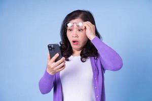 Portrait of middle aged Asian woman using smartphone on blue background photo