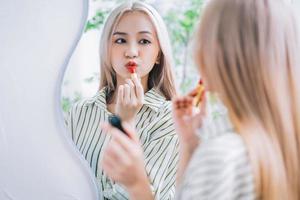 joven asiática aplicando lápiz labial frente al espejo