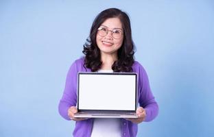 Portrait of middle aged Asian woman using laptop on blue background photo