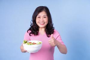 imagen de una mujer asiática de mediana edad comiendo ensalada con fondo azul foto