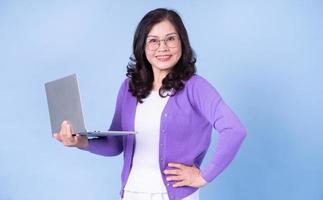 Portrait of middle aged Asian woman using laptop on blue background photo