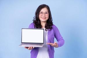 retrato de una mujer asiática de mediana edad usando una laptop con fondo azul foto