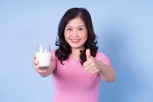 imagen de una mujer asiática de mediana edad bebiendo leche con fondo azul foto