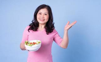 imagen de una mujer asiática de mediana edad comiendo ensalada con fondo azul foto