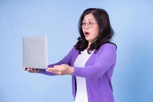 Portrait of middle aged Asian woman using laptop on blue background photo