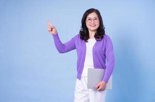 Portrait of middle aged Asian woman using laptop on blue background photo