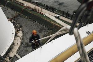 Trabajador de sexo masculino, altura inferior del tanque, placa de la carcasa, escalera de cuerda, acceso, inspección de seguridad del tanque de almacenamiento de espesor foto