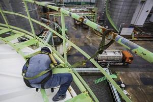 Male worker wearing safety first harness and safety lone working at high handrail place on top roof tank. photo