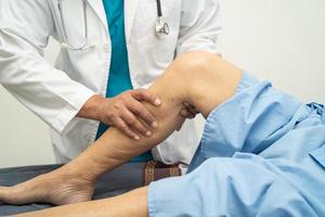 médico asiático fisioterapeuta que examina, masajea y trata la rodilla y la pierna del paciente mayor en el hospital de enfermería de la clínica médica ortopedista.