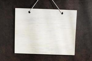 Blank white wooden sign hanging on dark textured wall. Mock up template photo