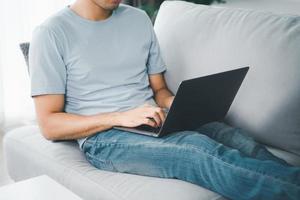 Young man sitting on the sofa at home typing on the laptop keyboard for online working, using internet, freelancer, relaxed, modern job lifestyle, work at home. photo