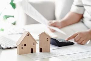 Woman calculate home loan mortgage to summary expense payments using calculator and laptop, with Small Wooden House Model, Planning to buy property, home loan concepts. photo