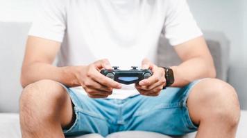 Excited young handsome man holding joystick controller playing video game sitting on the couch at home photo