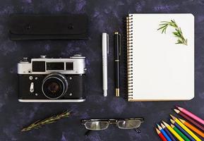 Flat lay, top view office table desk. Desk workspace with retro camera, diary, pen, glasses, case, rosemary on dark background. photo