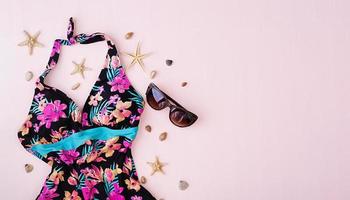 Swimsuit with different seashells and starfish on pink background. Top view photo