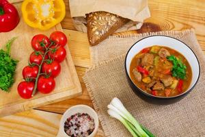 Stew with meat and vegetables in tomato sauce on wooden background photo