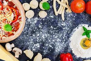 Raw pizza dough with ingredients and spices on dark background. Top view photo