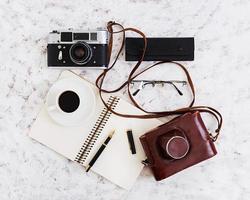 Flat lay, top view office table desk. Desk workspace with retro camera, diary, pen, glasses, case, cup of coffee on white background. photo