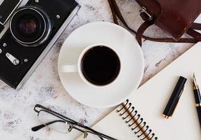 escritorio plano de oficina con vista superior. espacio de trabajo de escritorio con cámara retro, diario, bolígrafo, gafas, estuche, taza de café sobre fondo blanco. foto